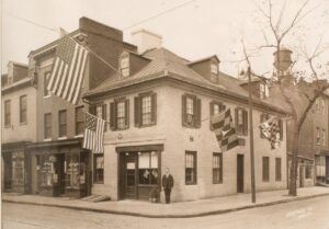 Sepia photograph of an early Baltimore street corner building decorated with American flags, circa late 1800s
